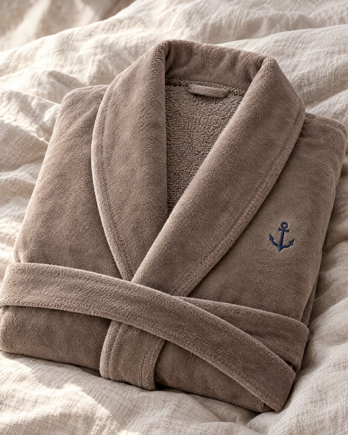 Peignoir velours taupe col châle plié sur un lit